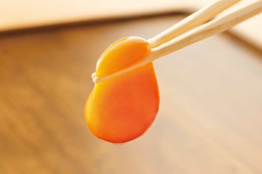 塚だま®を割り、黄身をお箸でつかんで持ち上げている写真。濃いオレンジで弾力感がある。