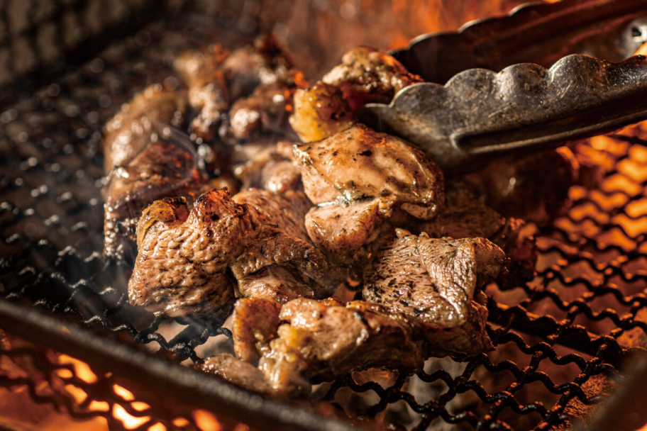 焼き上がりの地鶏もも肉と肉をつかんでいるトング。ジューシーな油と炭の黒が絡まって、シズル感のある美味しそうな写真